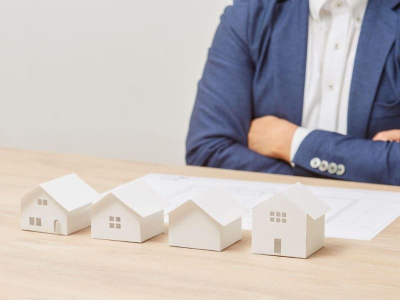 uomo seduto alla scrivania con davanti documenti e modellini di case